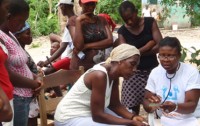 An staff member explains the contraceptive pill to a woman while girls watch